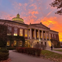 关闭-up view of a neoclassical government building with large columns and a facade made of stone. 几个旗帜, including the American flag, are visible in front of the building against a clear blue sky.