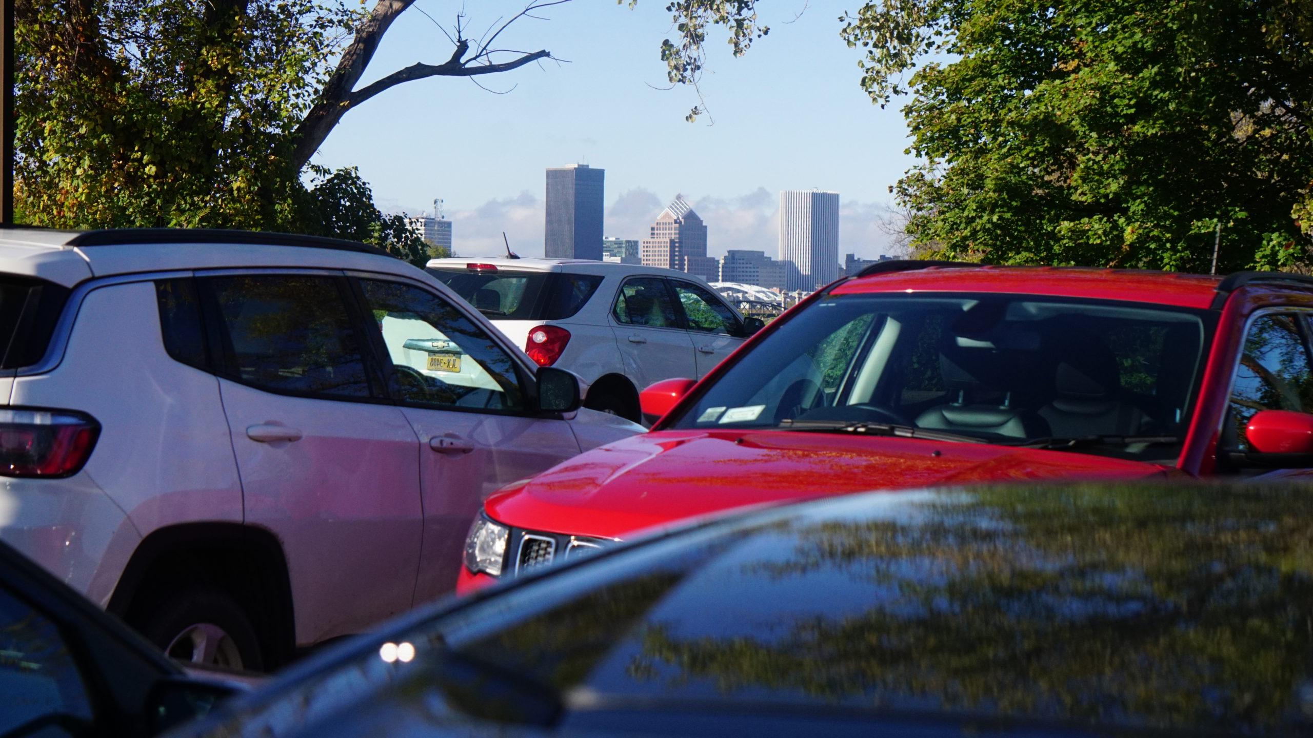 Red 和 white vehicles parked in lot with Rochester NY skyline in background